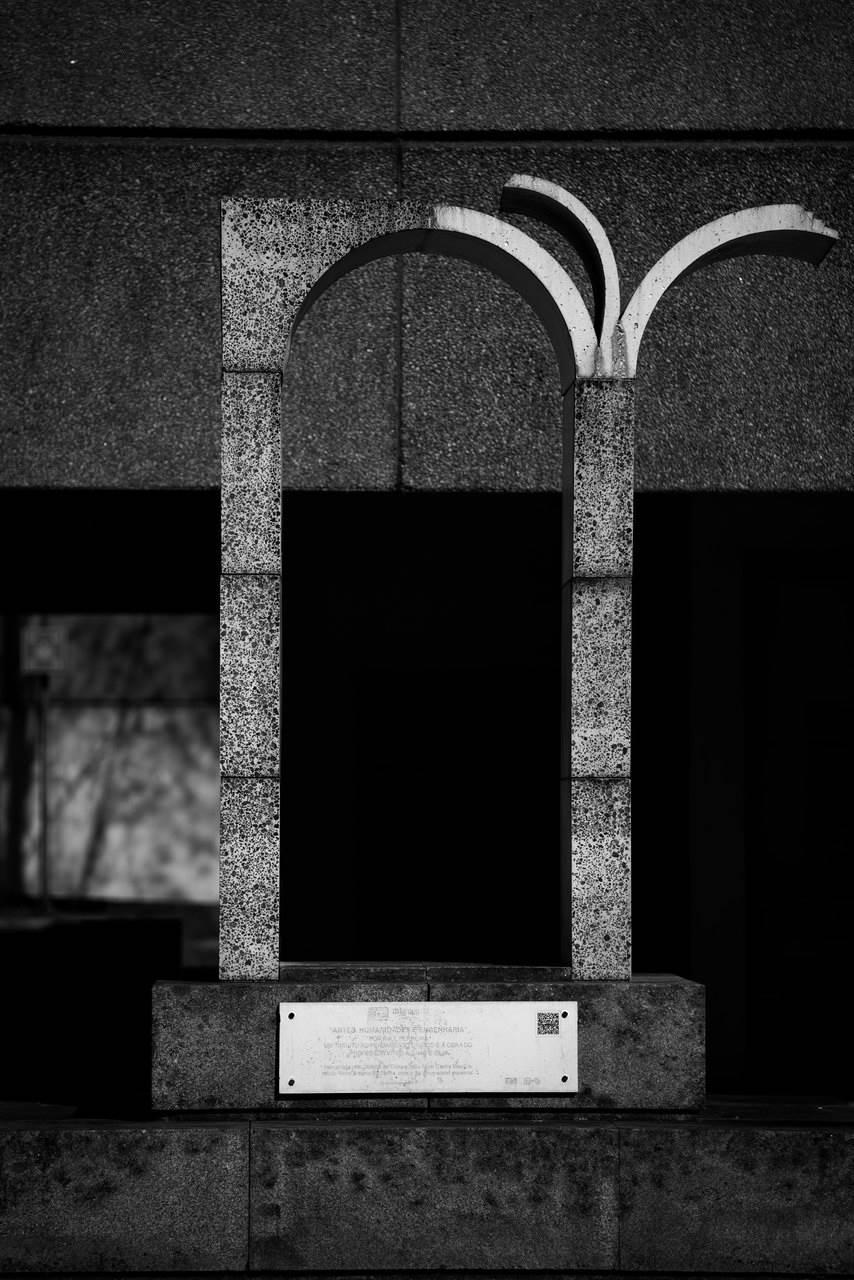 Placed in front of the, now, School of Letters, Arts and Human Sciences at the Gualtar Campus of the University of Minho, this work had the primary aim of honouring Vítor Aguiar e Silva (PT, 1939), Portuguese professor, writer and poet, winner of the Camões Prize in 2020 and one of the greatest national specialists in the work of Luís Vaz de Camões. The form, in an arch with a perfect curve, topped on the right side by a book, evokes classicism and the literature that corresponds to it. The project, an initiative of dstgroup and zet gallery, was joined by IB-S - Science and Innovation Institute for Bio-Sustainability of the University of Minho with the development of a mortar, equivalent to cement but made only of waste, which gave shape to the sculpture. The work thus unites the concepts of art, humanities, and engineering.
