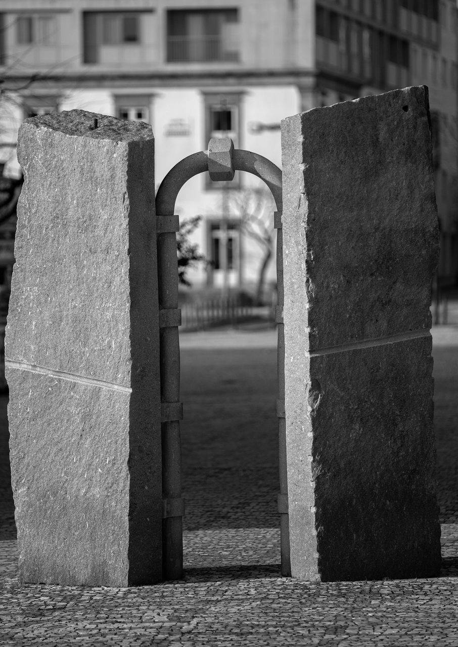 Isaque Pinheiro is one of the most outstanding sculptors of his generation, a maker and a transformer of the materials with which he creates illusions and ironies. In this work, two rectangular and irregular stone blocks, placed vertically and parallel to each other, are joined by a tube that simulates a perfect round arch in the Roman manner, evoking the city's history. The tube and the washers, which connect it to the stone blocks are also in granite, which highlights the effect of manipulation of the image and materials that the artist likes to use.